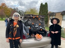 two women dressed for Halloween near truck decorated with spider webs and pumpkins